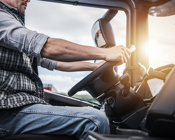A closeup of a truck driver seated in their truck holding onto the steering wheel. A closeup of a truck driver seated in their truck holding onto the steering wheel.