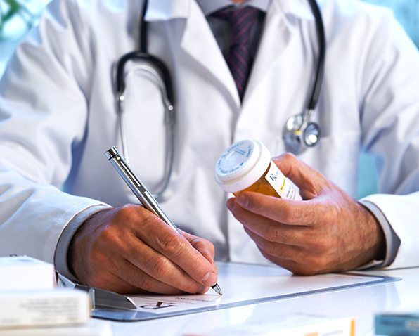A doctor writing a prescription while holding a bottle of pills. A doctor writing a prescription while holding a bottle of pills.