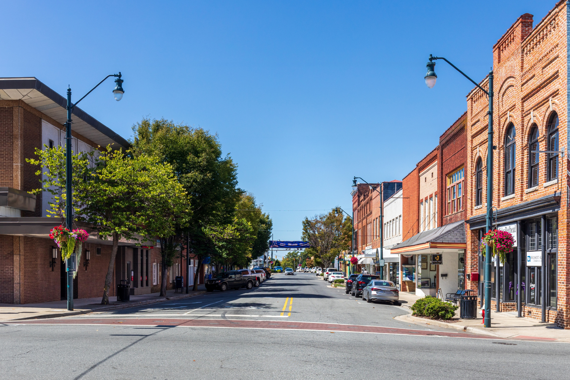 Downtown Asheboro, North Carolina, featuring a tree-lined main street with local businesses, historic brick storefronts, and parked vehicles.