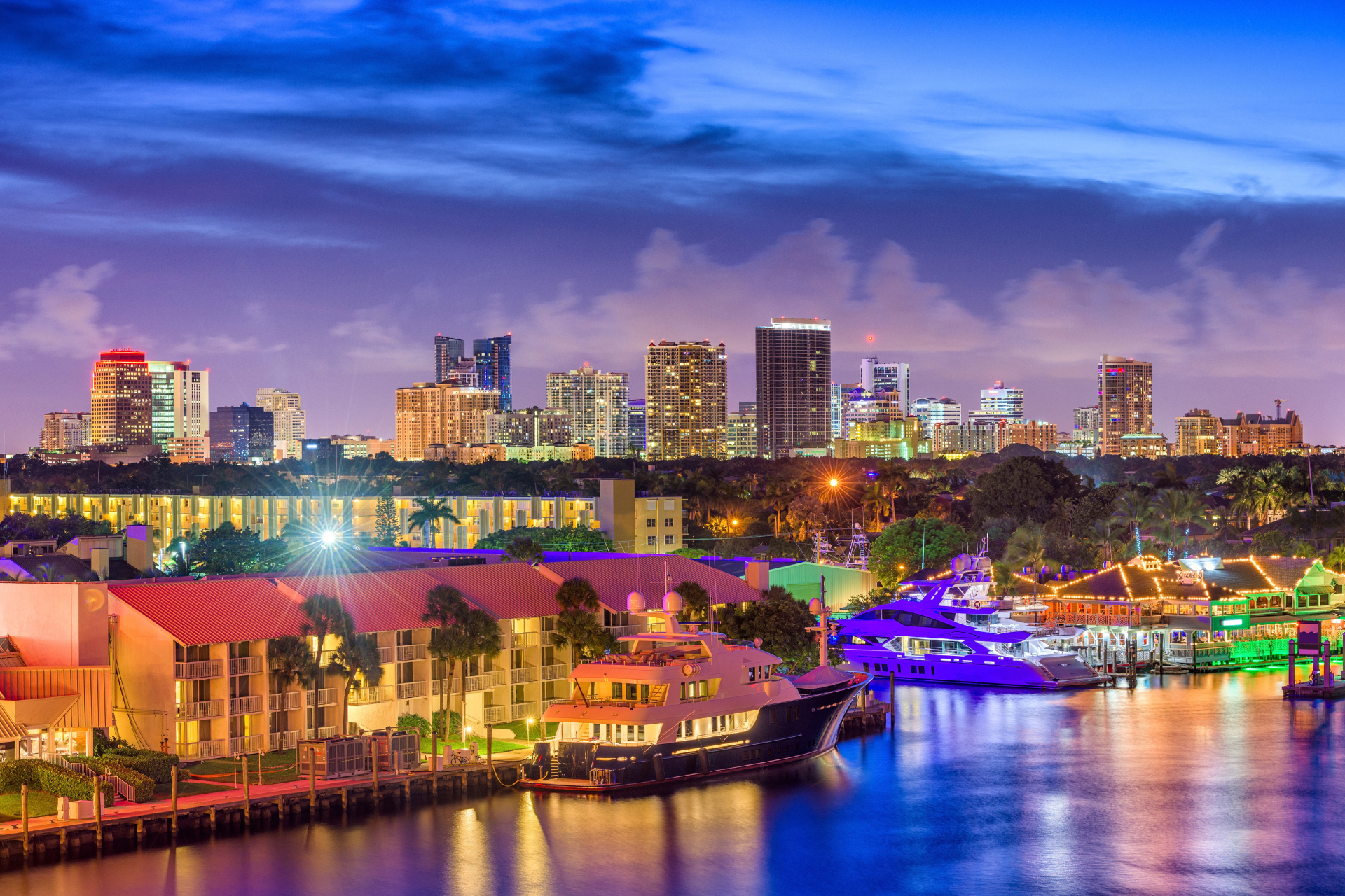 Fort Lauderdale, Florida waterfront at twilight, featuring a marina, yachts, city skyline, and colorful reflections along the Intracoastal Waterway.