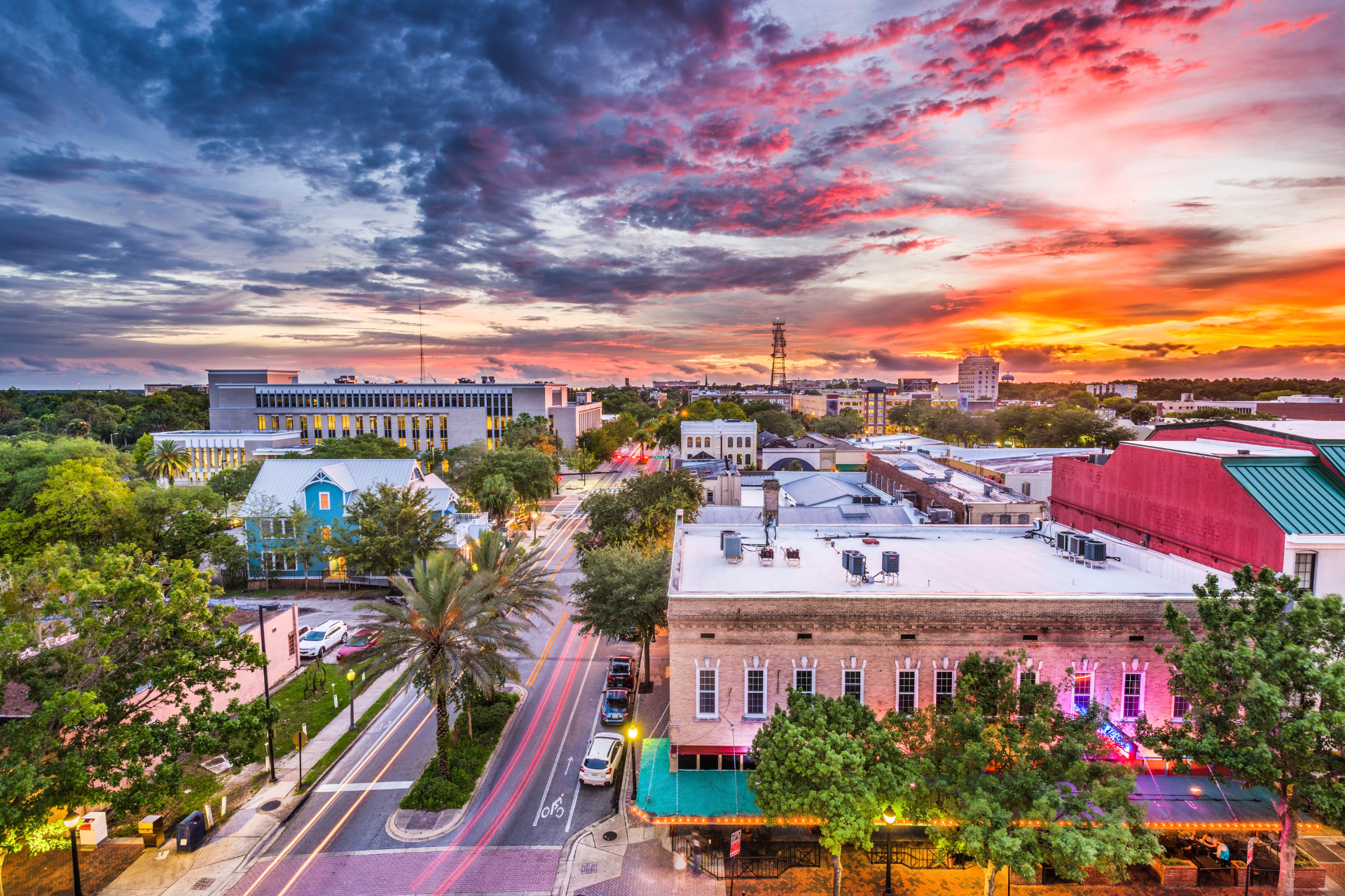 Downtown Gainesville, Florida at sunset, featuring historic buildings, tree-lined streets, and colorful clouds above the city skyline.
