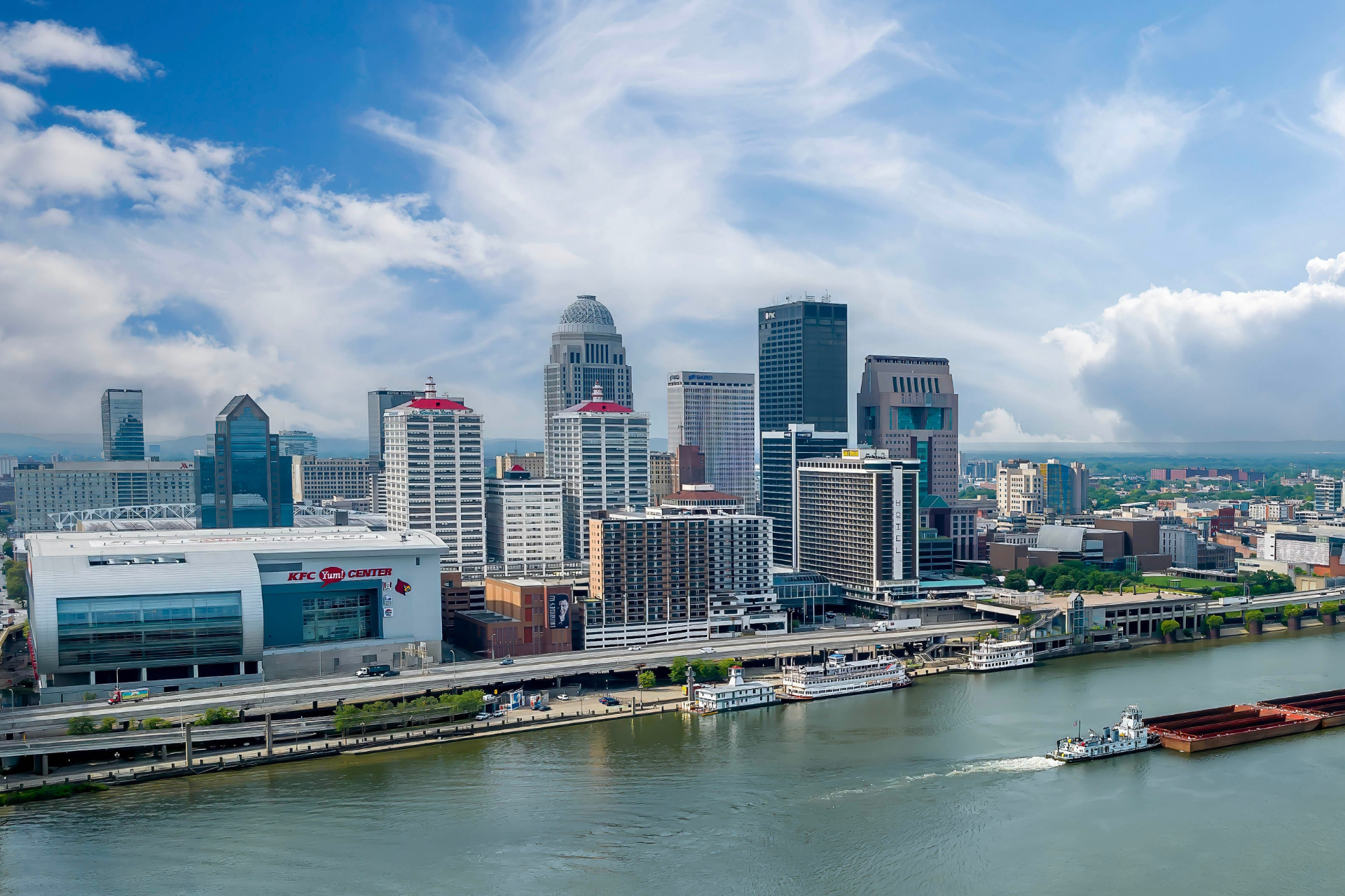 Skyline of downtown Louisville, Kentucky, along the Ohio River, featuring city high-rises, waterfront attractions, and river traffic.