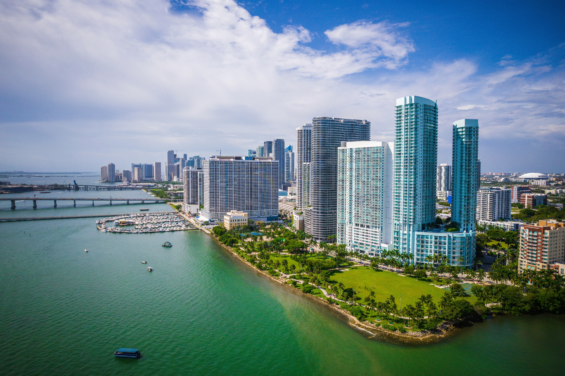 Aerial view of Miami, Florida skyline featuring modern waterfront high-rise buildings, Biscayne Bay, and a marina on a sunny day.