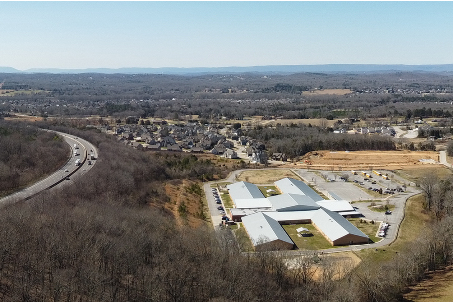 Aerial view of a suburban area in Ooltewah, Tennessee, with a large commercial building, nearby neighborhoods, and surrounding woodlands.