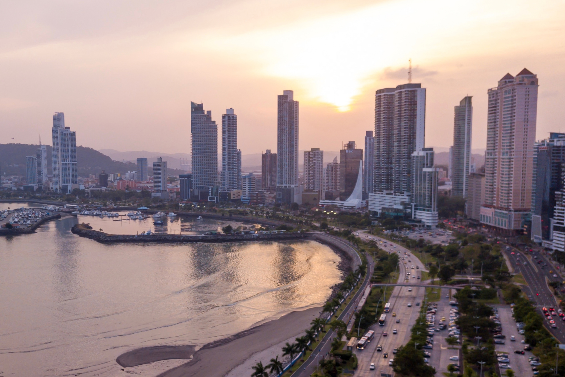 Coastal skyline of Panama City, Florida at sunset, with waterfront high-rise buildings, marina views, and a shoreline roadway.