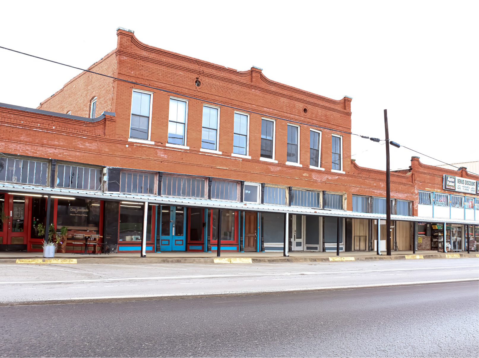 Historic red-brick storefronts with covered sidewalks along a quiet street in downtown Venus, Texas